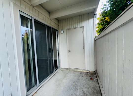 Private 1-bedroom patio with sliding glass door access, concrete flooring, exterior storage door, and fenced walls.