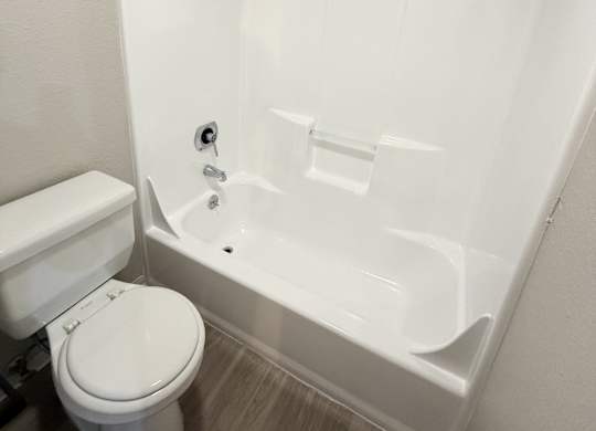 A white toilet sits next to a white bathtub in a small bathroom.