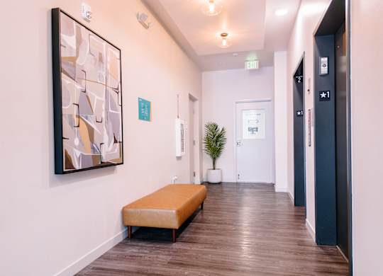 Hallway to elevators with a bench, a painting, and luxury vinyl plank flooring at Bode125 Seattle