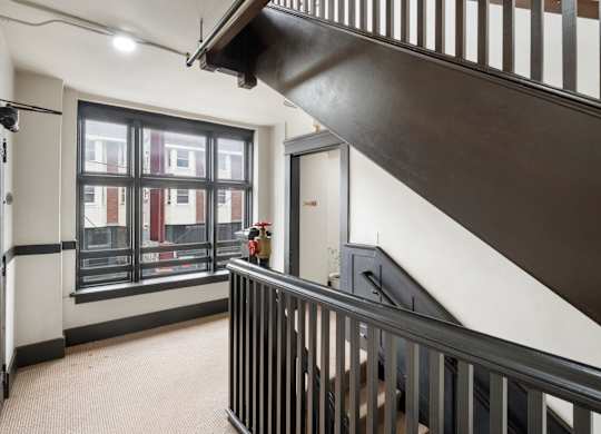 A black metal staircase with a white wall and a window with a view of a building.