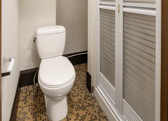 A white toilet in a small bathroom with a brown door.