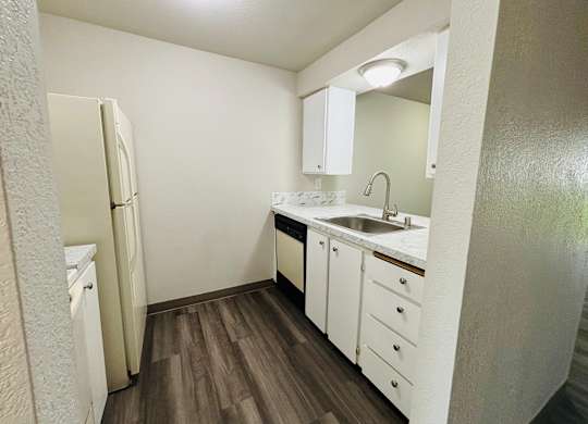 A small white kitchen with wood floors and a white refrigerator.