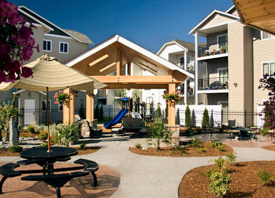 A playground area with a slide and picnic tables is surrounded by apartment buildings.