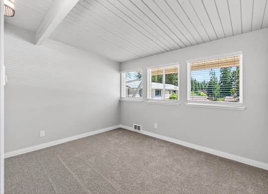 A room with a carpeted floor and a window showing a view of trees and a house.