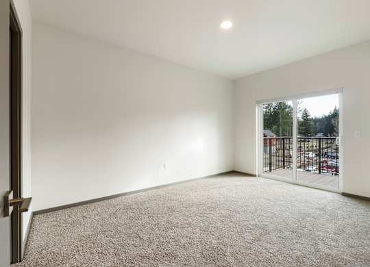 A room with a carpeted floor and a sliding glass door leading to a parking lot.