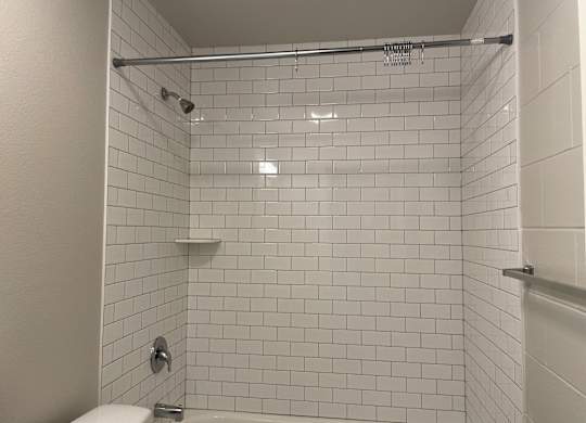 A white tiled shower with a white toilet and a white shower head.