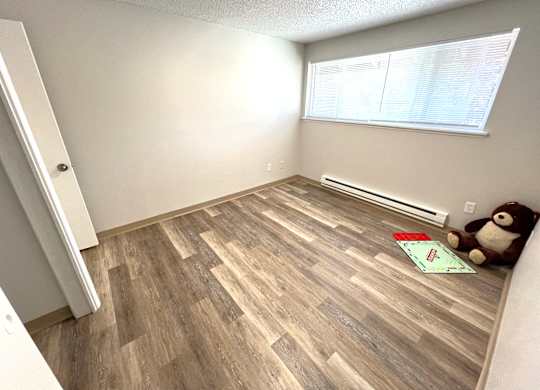 A room with wooden flooring and a teddy bear on the floor.