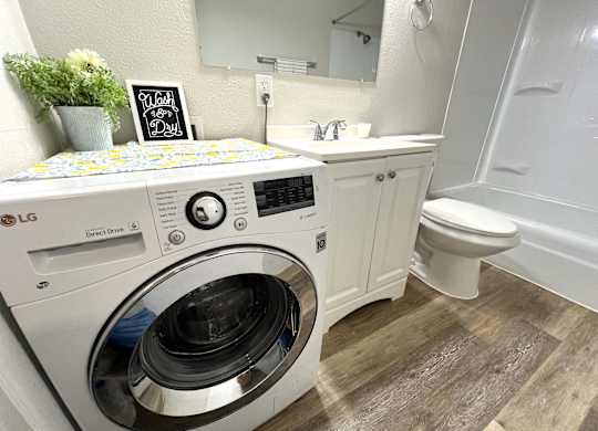 A washing machine is on top of a washbasin in a bathroom.
