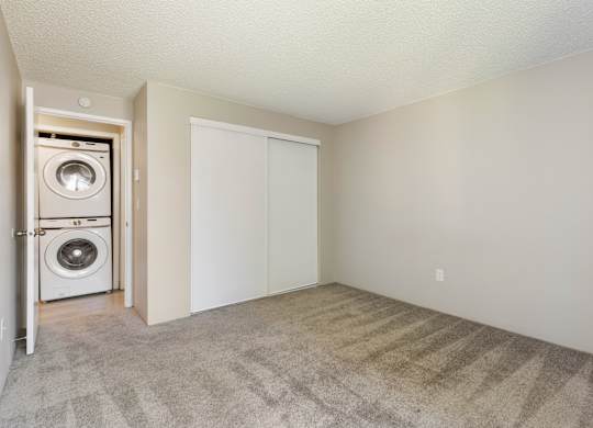 A bedroom with a closet and carpet. Across the hallway from a washer and dryer.