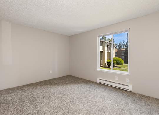 A bedroom with a window, baseboard heater and carpet