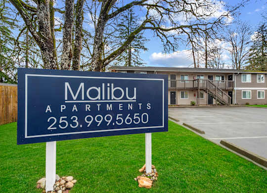 A blue sign for Malibu Apartments stands in front of a building.
