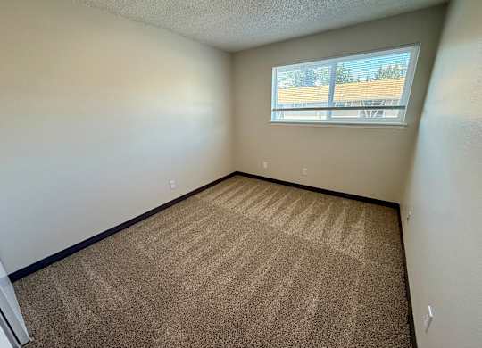 A room with a carpeted floor and a window showing a view of a parking lot.