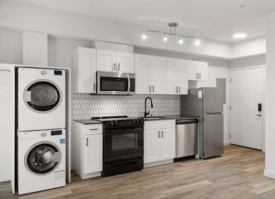 Modern studio apartment at Bode-88 in Seattle with stainless steel appliances, in-home washer and dryer, white shaker cabinets, and tile backsplash