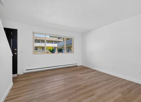 A room with wooden flooring and a large window showing an outdoor view.