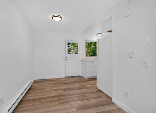 A white room with wood flooring and a window.