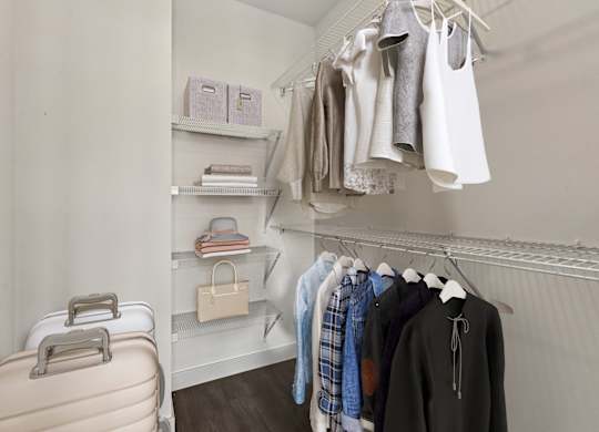 A suitcase is on the floor next to a closet with clothes hanging.