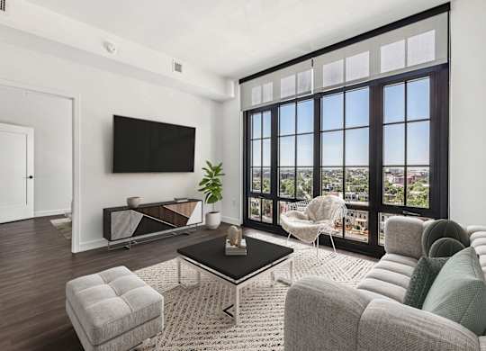 A living room with a flat screen TV mounted on the wall and a large window with a view of the city.