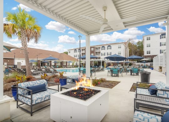 an outdoor patio with a fire pit and chairs and umbrellas at The Met Apartment Homes, Hattiesburg, MS, 39402