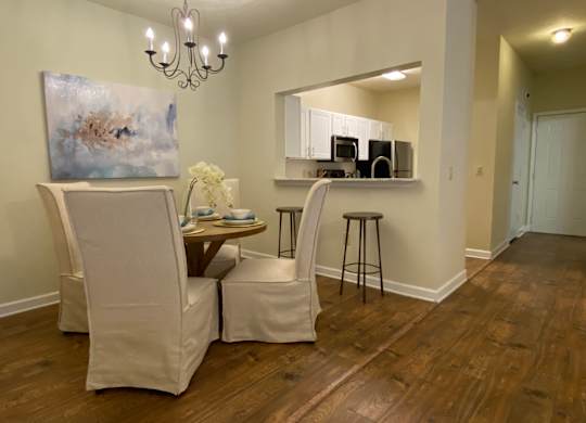 A room with a painting, a chair, a table with a vase of flowers, and a bar area with stools.