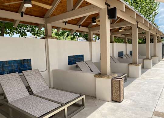 A row of sun loungers are lined up under a wooden roof.