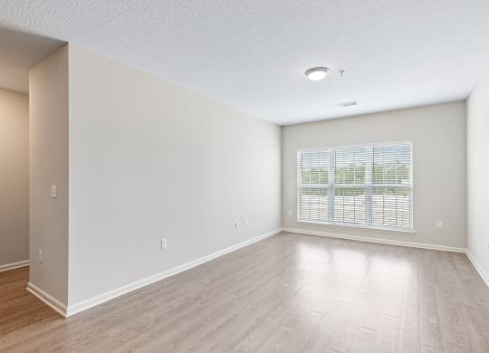 an empty living room with a large window and wood flooring at The Met Apartment Homes, Hattiesburg