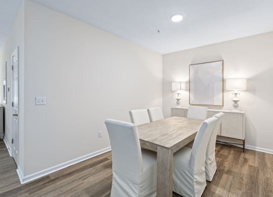 a dining room with a wooden table and white chairs at The Met Apartment Homes, Hattiesburg
