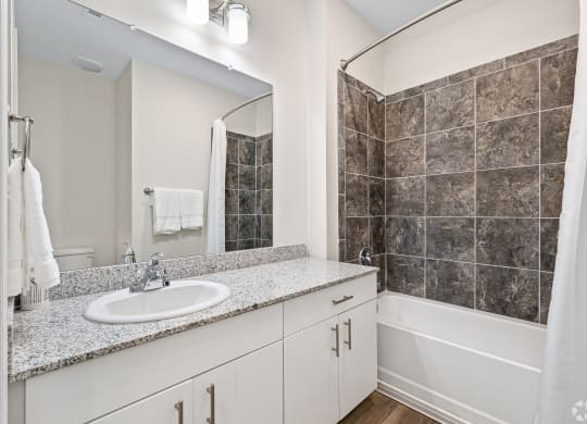 a bathroom with a sink and a shower and a mirror at The Met Apartment Homes, Hattiesburg, MS