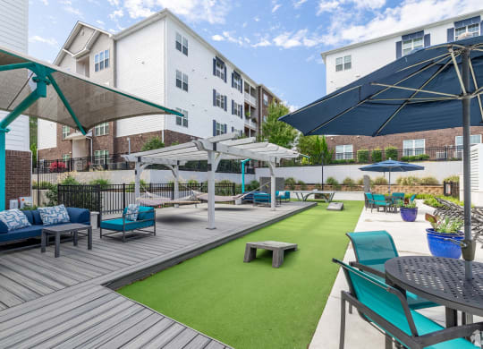 a patio with blue chairs and umbrellas and a green turf at The Met Apartment Homes, Hattiesburg, Mississippi