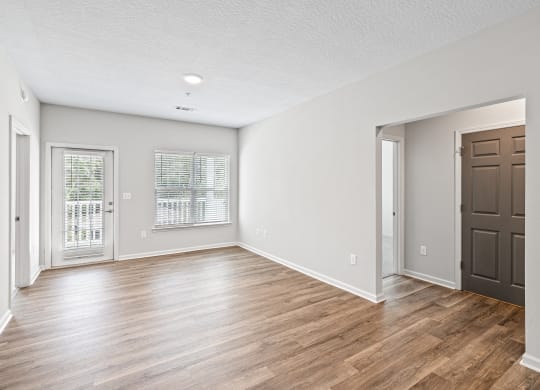 an empty living room with wood flooring and a brown door at The Met Apartment Homes, Mississippi 39402