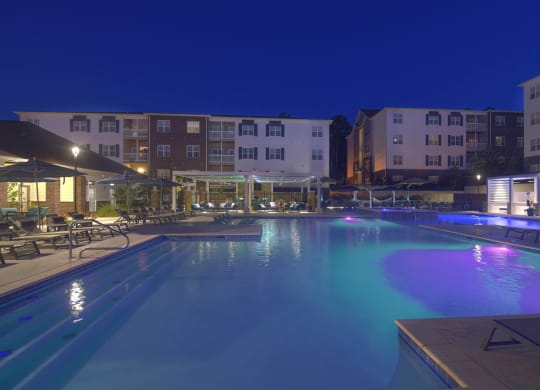 A large swimming pool lit up with blue and purple lights at night at The Met Apartment Homes, Hattiesburg, MS
