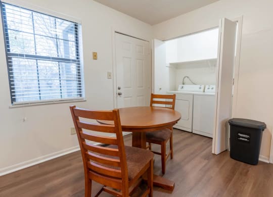a dining area with a table and chairs and a laundry room in the background
