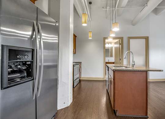 A modern kitchen with a stainless steel refrigerator and wooden cabinets. at 100 South Apartments, Buffalo, NY 14202