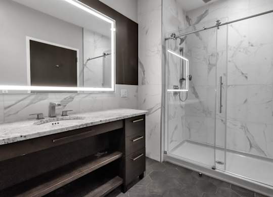 A modern bathroom with a walk-in shower and a vanity with a marble countertop.