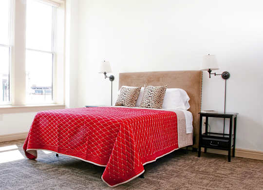 a bedroom with a bed with a red blanket and two windows at 100 South Apartments, Buffalo, New York