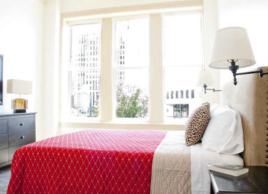 a bedroom with a red bed and three windows at 100 South Apartments, New York, 14202