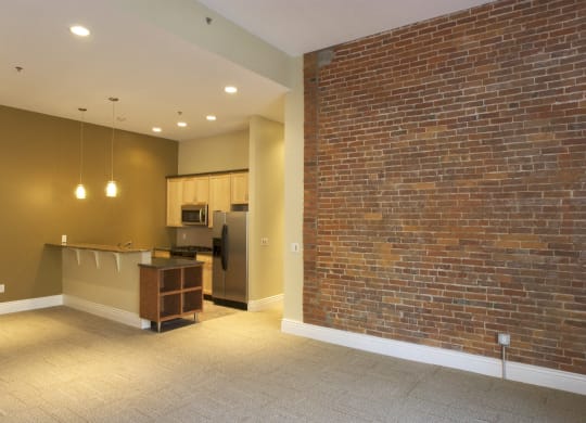 an empty living room with a brick wall and a kitchen at The Granite Works Apartments , New York 14202