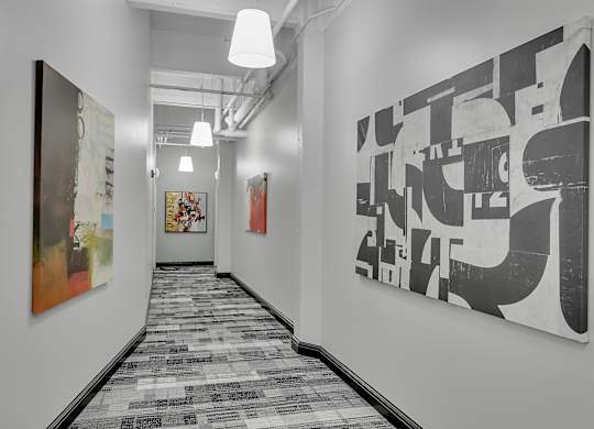 a long corridor with paintings on the wall and a hallway with a patterned carpet at 100 South Apartments, Buffalo, 14202