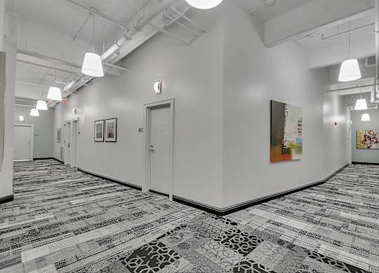 a long hallway with white walls and tiled floors and a door at 100 South Apartments, Buffalo, New York