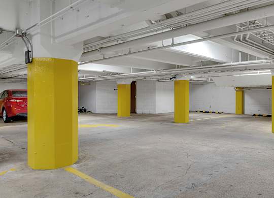 a parking garage with yellow pillars and a red car at 100 South Apartments, New York, 14202