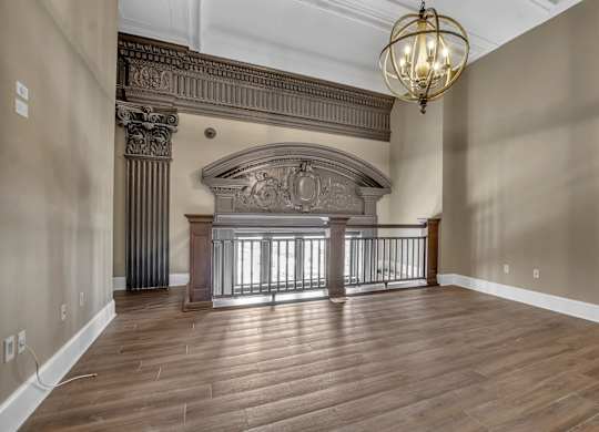 A large, empty room with a wooden floor and a chandelier hanging from the ceiling at The Knights @ 506 Delaware Apartments, New York, 14202