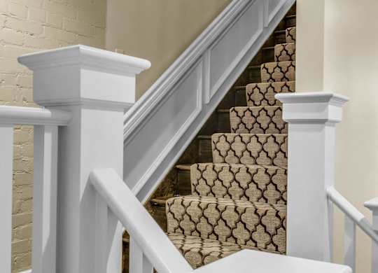 A staircase with a beige carpeted runner and white railings at The Knights @ 506 Delaware Apartments, Buffalo, NY