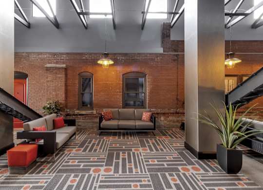 a lobby with couches and a rug in front of a brick wall at The Knights @ 506 Delaware Apartments, Buffalo, 14202