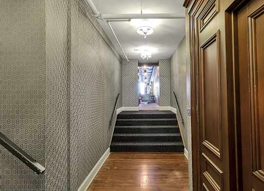 a long hallway with stairs and wood flooring and a hallway with doors and stairs at The Knights @ 506 Delaware Apartments, Buffalo, 14202