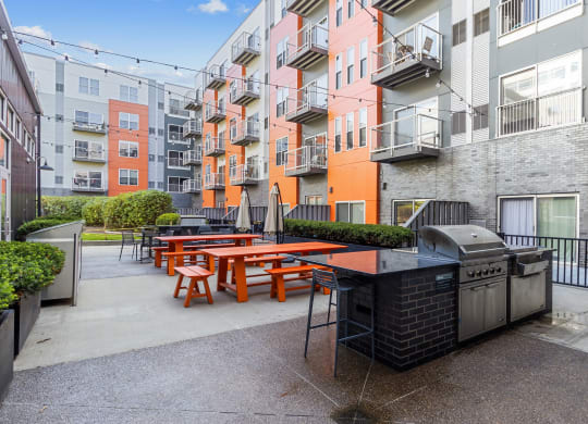 an outdoor patio with picnic tables and a grill in front of an apartment building at Bakery Living, Pittsburgh, PA