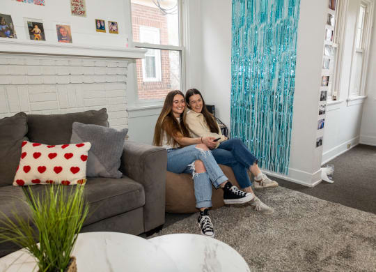 two girls sitting on a couch in a living room at University Commons Apartments, Oakland, Pittsburgh