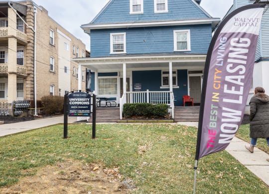 a woman walks past a blue house with a purple banner in front of it at University Commons Apartments, Oakland, Pittsburgh