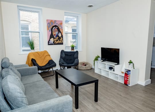 a living room with a couch coffee table and chairs and a tv on a stand at University Commons Apartments, Oakland, Pittsburgh