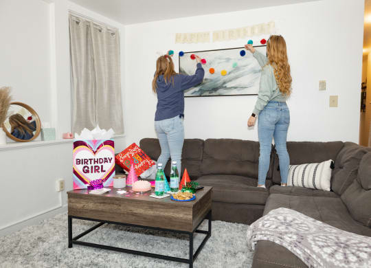 two girls hanging a happy birthday banner on a wall in a living room at University Commons Apartments, Oakland, Pittsburgh