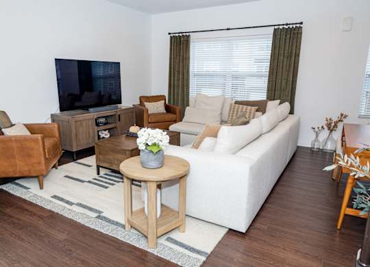A living room with a white couch, a brown leather chair, a wooden coffee table, and a flat-screen TV. at Highland Village, Ross Township, Pittsburgh, PA 15229