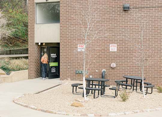 A woman stands in the doorway of a brick building with a sign at Walnut Towers at Frick Park, Pittsburgh, 15217